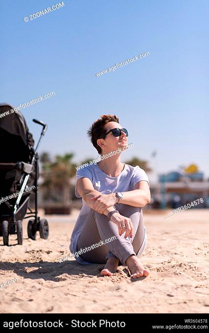 Young mother with sunglasses relaxing on beach with baby stroller outdoor