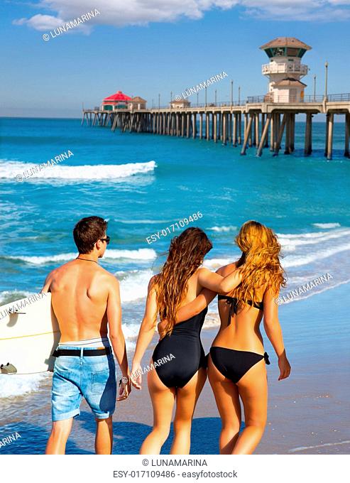 Teen surfers group of boys and girls walking rear view on Huntington beach California