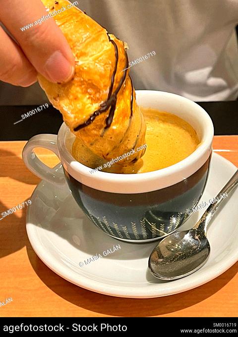 Hand dipping a minicroissant in a cup of coffee