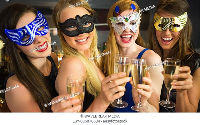 Smiling friends holding champagne glasses wearing masks