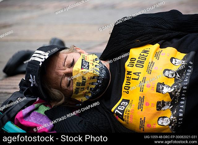 A mother of a relative killed during the flase positives lays on the ground with a shirt and a face mask that reads ""Who gave the order?"" with photos of army...