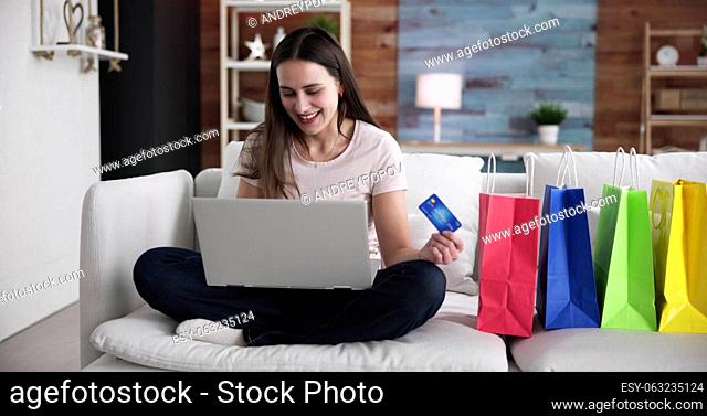 Young Woman Sitting On Sofa Shopping Online With Shopping Bags