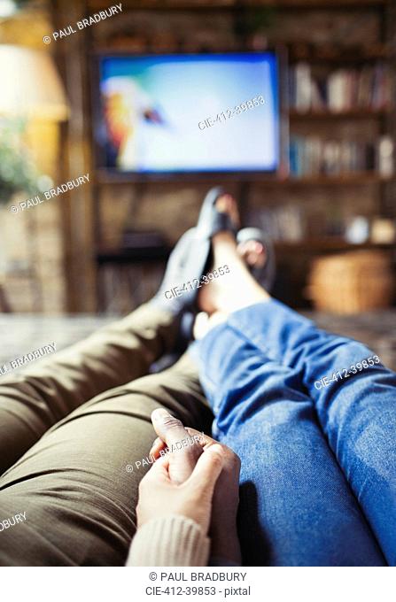 Personal perspective affectionate couple holding hands watching TV in living room