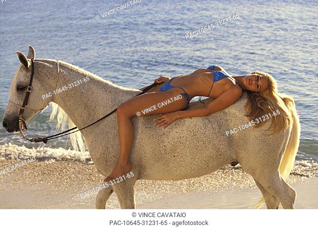 Blonde woman in bikini laying on horseback