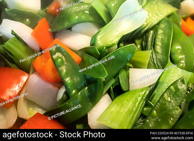 23 May 2022, Baden-Wuerttemberg, Rottweil: Sugar snap peas, red bell peppers, kohlrabi and pak choi are cooked in a wok. Photo: Silas Stein/
