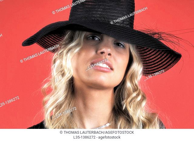 Young blonde woman in a black hat against a red background