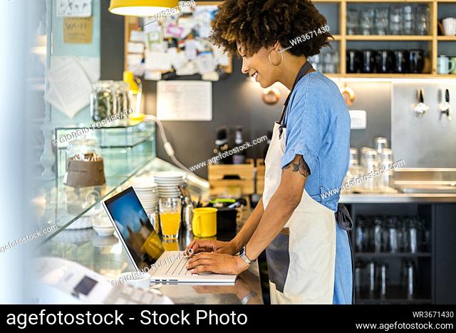 Female owner using laptop at counter in coffee shop