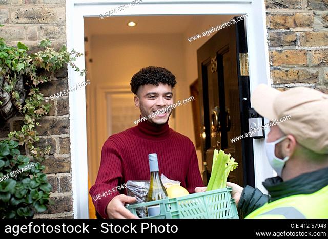 Happy man receiving grocery delivery from delivery man in face mask