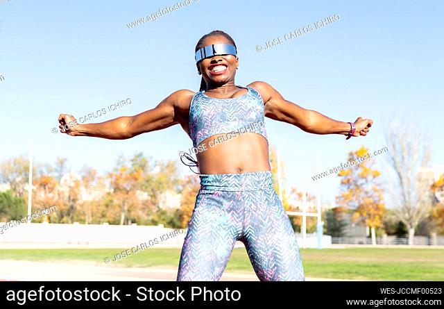 Cheerful female athlete in sunglasses jumping against clear sky on sunny day