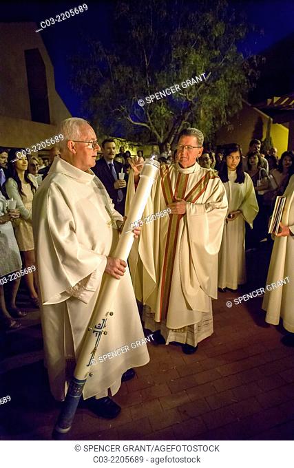 The robed pastor of St. Timothy's Catholic Church, Laguna Niguel, CA, lights the Easter candle held by an elderly deacon beside the Easter fire at the start of...