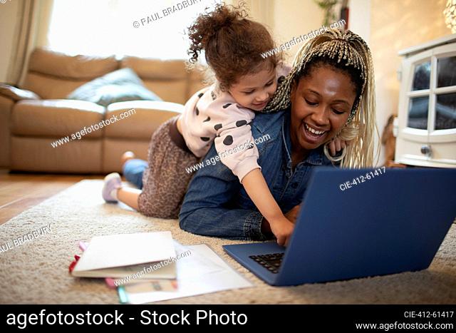 Curious daughter watching mother working at laptop on floor
