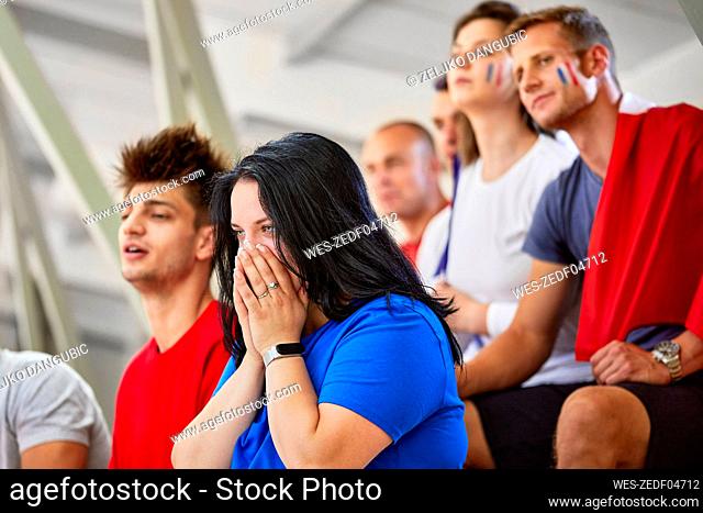 Woman with hands covering mouth expressing disappointment at sports event in stadium