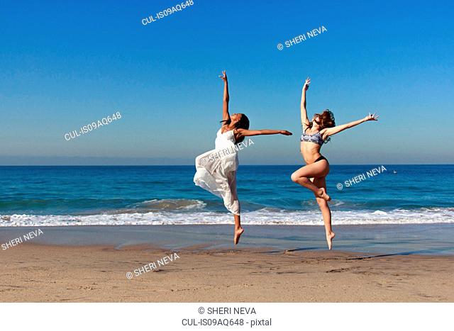 Two young female dancers leaping mid air on beach