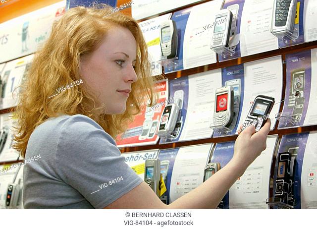 Young woman looking at mobile phones of various manufacturers in a shop. - BONN, GERMANY, 15/02/2005
