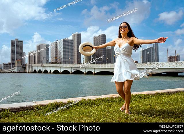Happy young woman spinning on grass by bay against sky