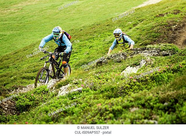 Young male and female mountain bikers cycling on hillside track