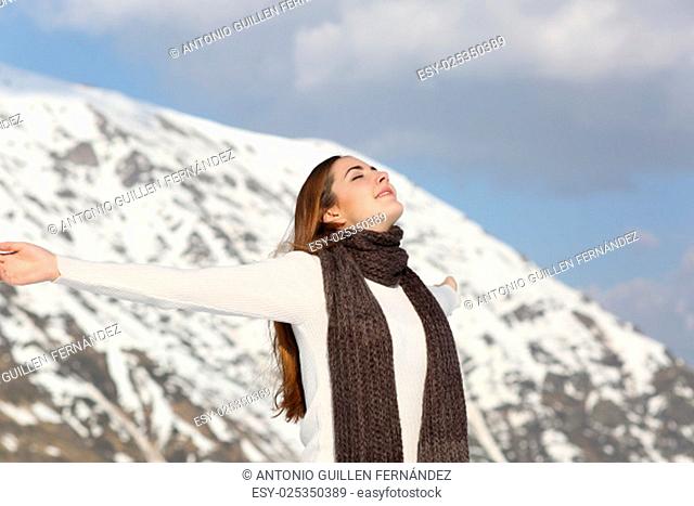Woman breathing fresh air raising arms in winter with a snowy mountain in the background