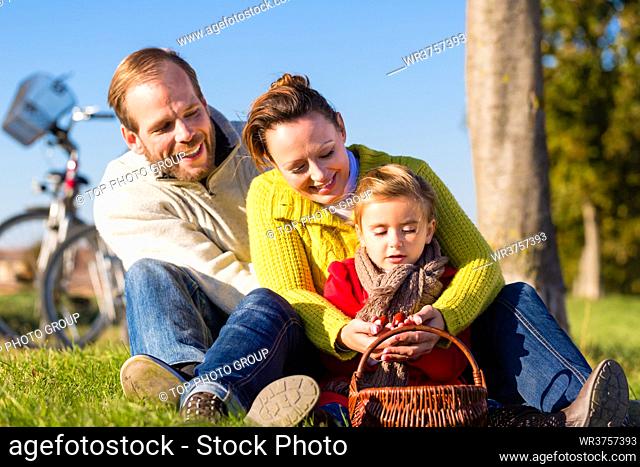 Family with mother, father and daughter having family trip on bicycle or cycle in park or country collecting chestnuts