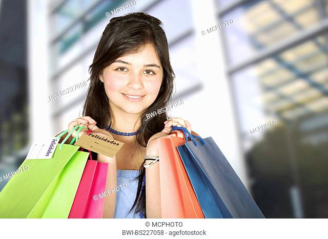 young girl in front of shopping centre holding up shopping bags with a smile