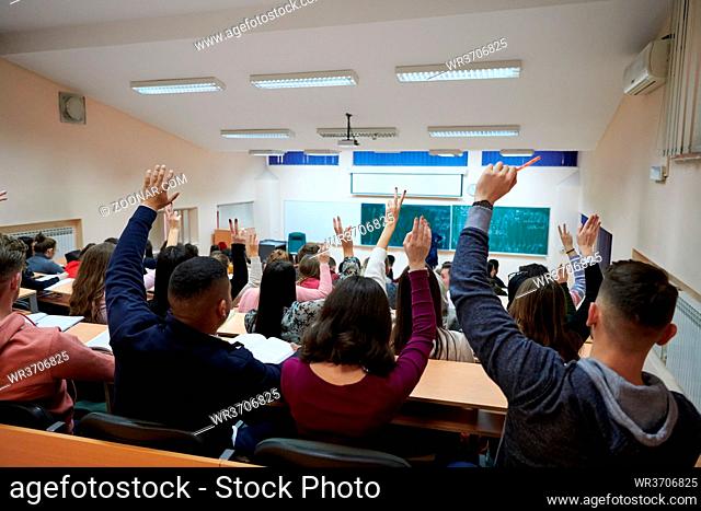 a large group of students raises their hand to answer a question asked by the professor