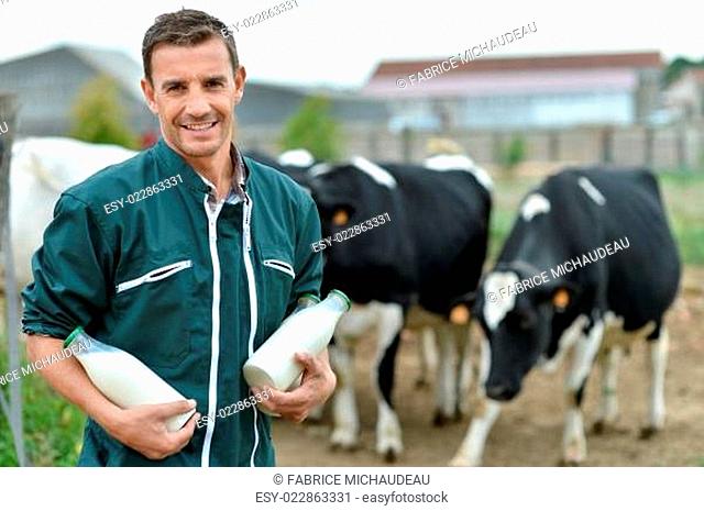 Farmer standing in front of cow herd with bottles of milk