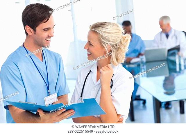 Two young doctors talking about a blue file in front of two doctors