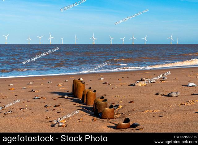 North sea coast in Caister-on-Sea, Norfolk, England, UK - with a wave breaker at the beach and wind turbines in the background