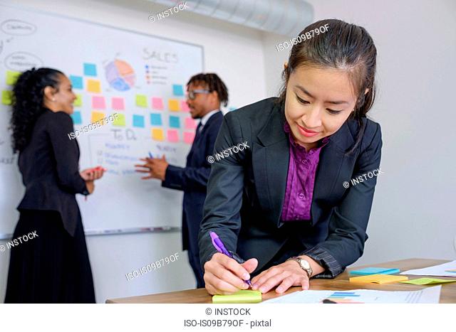 Businessman and businesswomen, in office, brainstorming, sticking notes to whiteboard