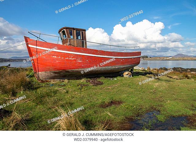 Ireland, Galway, 2016/04 , A red derelict wooden fishing boat lies decaying on the shoreline of the Irish coast.