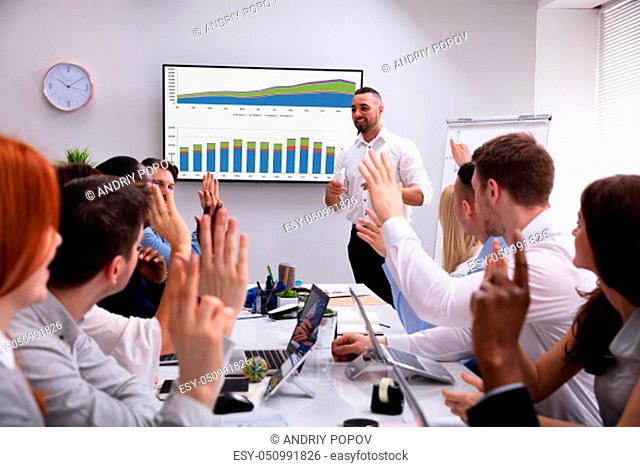 Group Of Multi Ethnic People Clapping For A Successful Businessman Giving Presentation On Screen