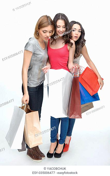 Full length portrait of three nice girls wearing shirts and jeans looking at their wonderful bootees. Isolated on the white background