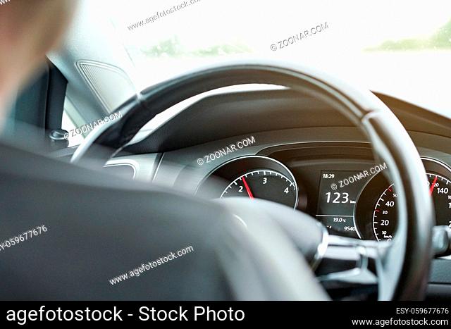 Man driving a car, view from back seat, detail on dashboard and steering wheel