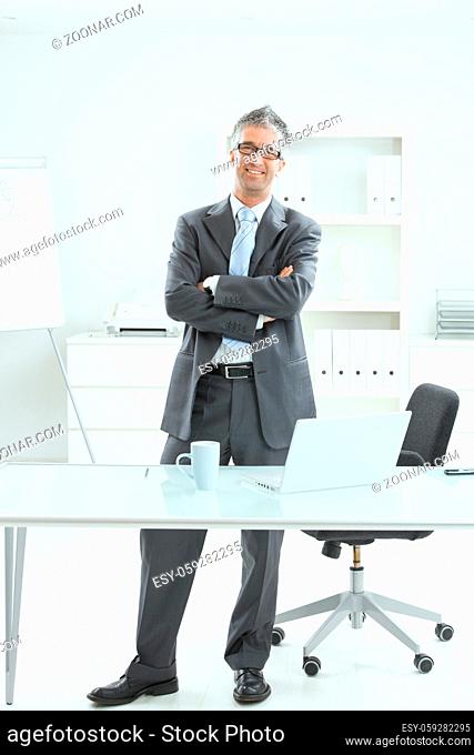 Happy businessman standing at office desk, smiling