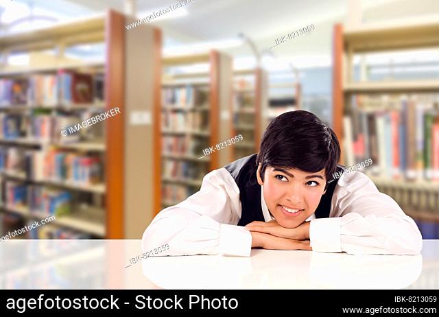 Young female mixed-race student daydreaming in library looking to the left