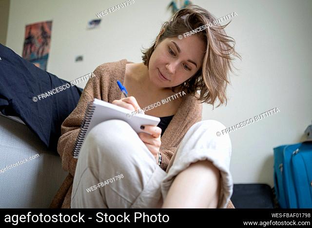 Woman with brown hair drawing on book while sitting in front of bed at home