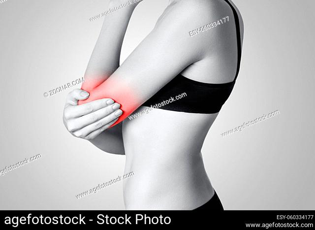 Closeup view of a young woman with elbow pain on gray background. Black and white photo with red dot