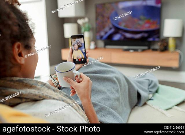 Woman with tea video chatting with parents on smart phone screen