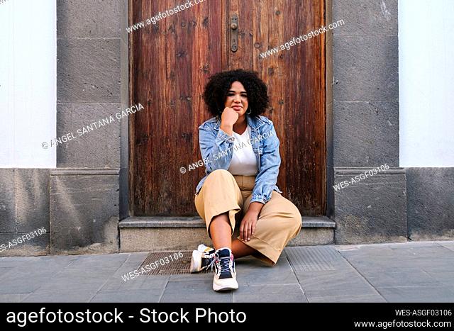 Young woman with hand on chin sitting in front of wooden door