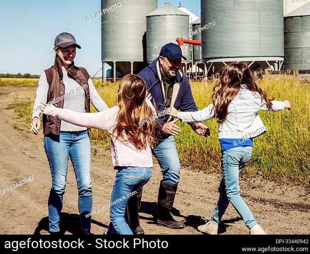 Two young girls running to greet their parents on their family farm with grain bins in the background; Alcomdale, Alberta, Canada