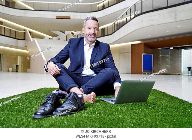 Businesssman sitting on synthetic turf using laptop