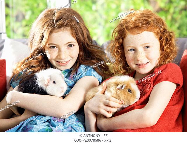 Girls holding pet hamsters in living room