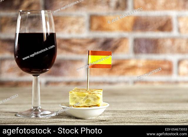Spanish omelette brochette with spanish flag and red wine glass on wooden table and red brick background