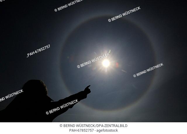A young woman pointing towards a sun halo in the sky in Purkshof, Germany, 29 April 2016. PHOTO: BERND WUESTNECK/dpa | usage worldwide