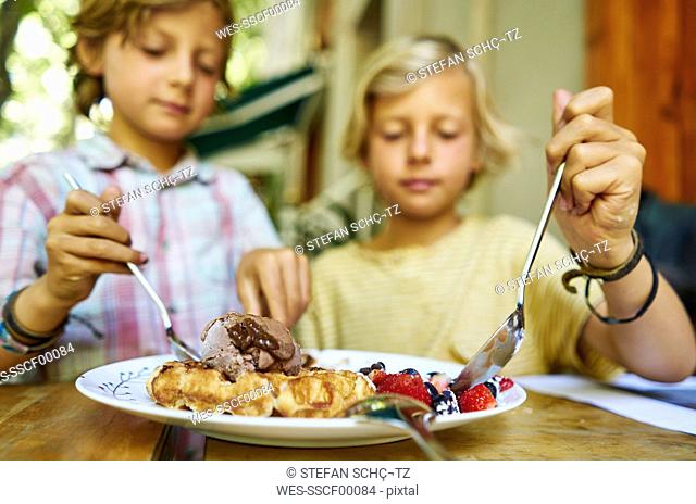Two boys sitting at table eating ice cream