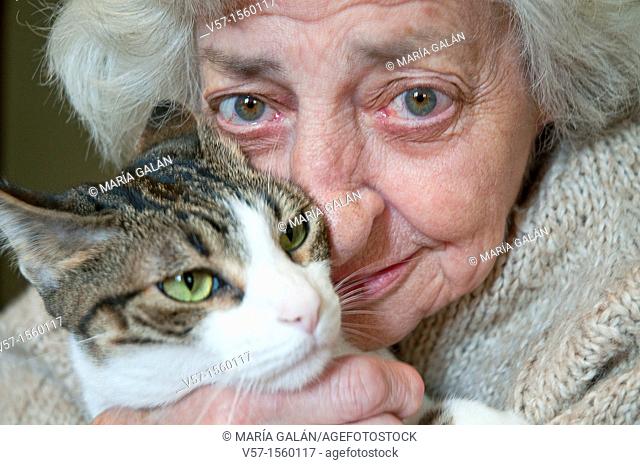Portrait of old woman hugging her cat, looking at the camera. Close view