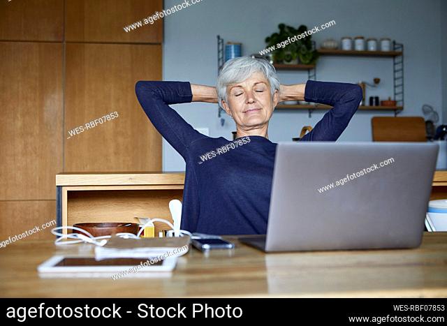 Senior woman with hands behind head relaxing while sitting at home