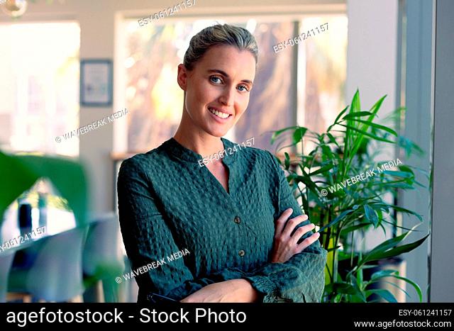 Portrait of smiling caucasian businesswoman with arms crossed standing at modern workplace