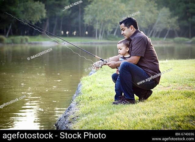 Happy young ethnic father and son fishing at the lake