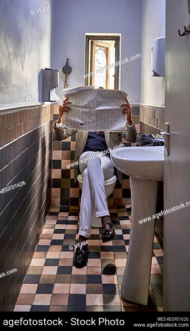 Stylish young businessman reading the newspaper sitting in the restroom