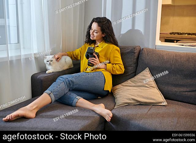 Pet owner. Pretty dark-haired woman with camera stroking her white cat
